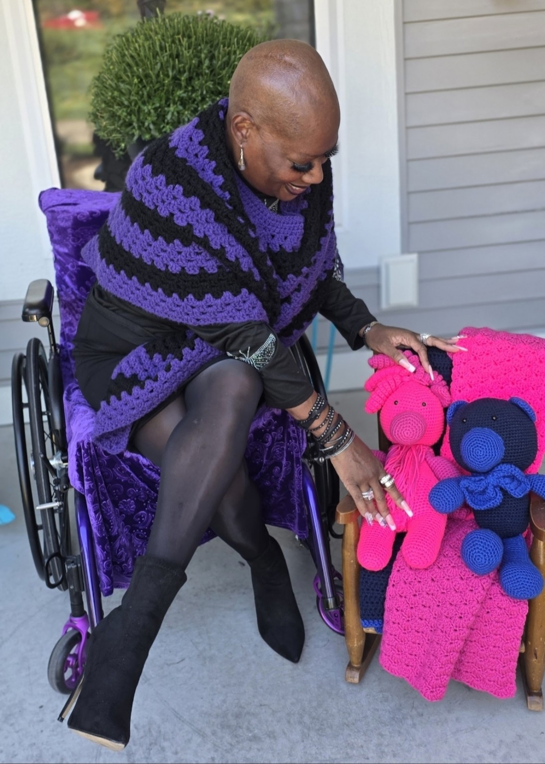 Dr. Kimberly leans toward a small wooden chair displaying Shana’s pink and blue crocheted bears and matching crochet pieces.